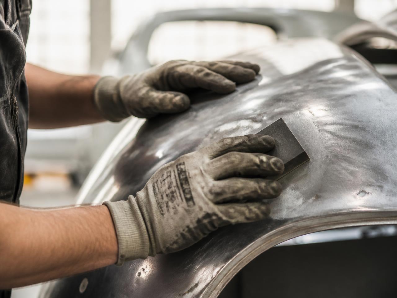 Manos con guantes de trabajo puliendo la chapa de un vehículo clásico durante su restauración